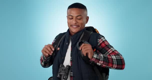 Black man, face and hiking with backpack, travel and smile in studio with mockup space isolated on blue background. Adventure, ready to go trekking and fitness, camper or hiker explore in portrait. - Footage, Video