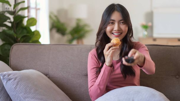 Las mujeres que comen pan mientras ven la televisión y cambian de canal con control remoto en el estilo de vida en casa. - Foto, imagen