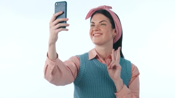 Felice, social media e segno di pace selfie con una donna in studio su sfondo blu per una foto profilo. Telefono, sorriso e foto con un giovane influencer o creatore di contenuti in posa per un aggiornamento di stato. - Filmati, video