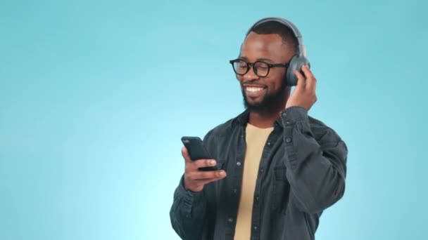 Black man, headphones and dancing studio with music, radio or audio with happiness on blue background. Listen, smile and person with digital media streaming hip hop, sound or podcast for freedom. - Footage, Video
