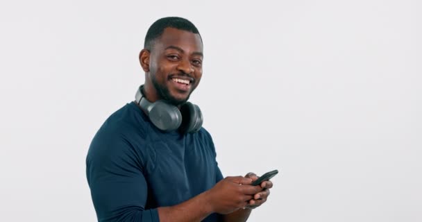 Słuchawki, telefon i portret mężczyzny w studio do streamingu muzyki i audio lub dźwięku. Happy African mężczyzna osoba na białym tle ze smartfonem do subskrypcji online i sieci. - Materiał filmowy, wideo