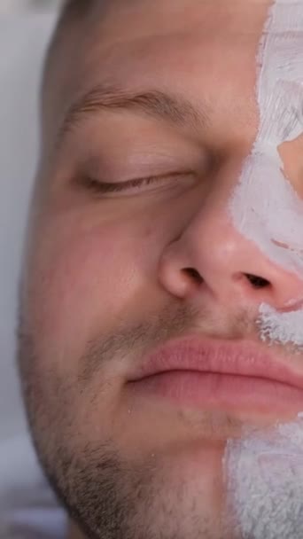 Close-up de uma cara de homem enquanto coloca uma máscara em uma cara de homem. Um homem numa consulta com um cosmetologista, um dermatologista. Cuidado da pele dos homens. Vídeo vertical - Filmagem, Vídeo