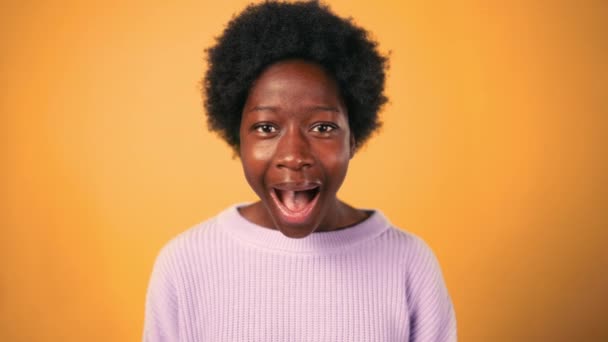 Een Afro-Amerikaanse vrouw met krullend haar opent haar mond in shock, toont de emotie van verrassing, geïsoleerd tegen een oranje achtergrond. - Video