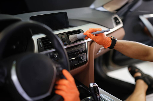 Мужчина держит серый румянец в оранжевых защитных перчатках. Подробная концепция химчистки автомобиля - Фото, изображение