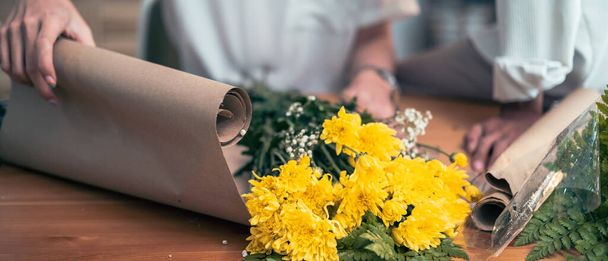 Önlüklü kadın çiçekçi kağıt üzerinde ahşap bir masa üzerinde beyaz gül buketi düzenliyor, paketliyor. - Fotoğraf, Görsel