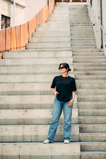 Belo tiro de comprimento total de uma mulher sorridente sentada em escadas de concreto ao ar livre. - Foto, Imagem