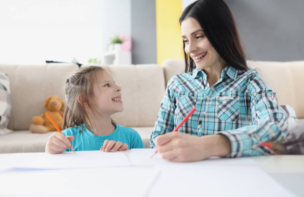 Feliz mamá y su hija dibujan con lápices sobre papel. Desarrollo de habilidades creativas del concepto de niños - Foto, Imagen