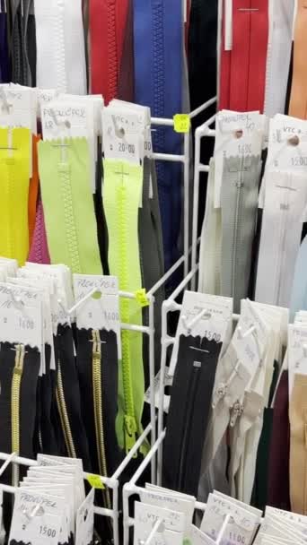 Wiele różnych zamków błyskawicznych na ubrania w różnych rozmiarach i kolorach, błyskawice umieszczane są na regałach w warsztacie pracowni odzieżowej. Pionowe wideo - Materiał filmowy, wideo