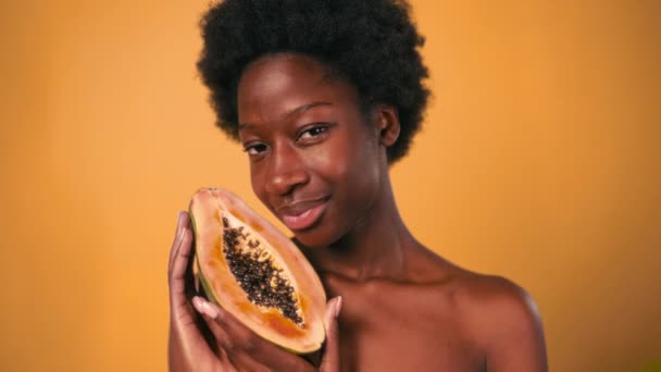 Afrikai-amerikai fiatal nő afro haj tartja papaya a kezében elszigetelt narancs háttér. Bőrápolás és gyógykezelések. - Felvétel, videó
