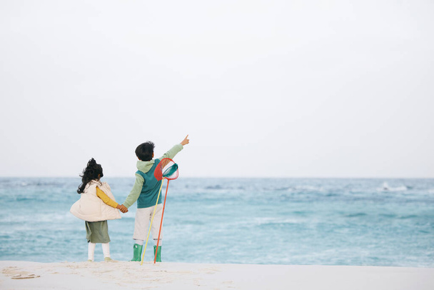 Rodzina, plaża i dzieci wskazujące na fale, niebo lub ocean dla rozwoju dziecka i uczenia się o wodzie na przestrzeni makiety. Morze, brat i siostra na piasku dla wolności, przygody i podróży wakacyjnej. - Zdjęcie, obraz