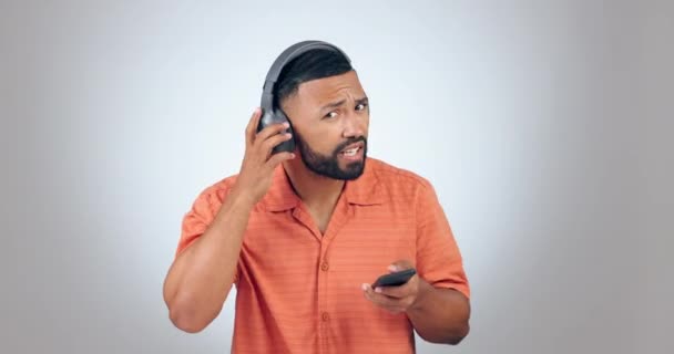 Listening, music and a man with a phone on a studio background for radio, streaming or fun. Happy, hear and a person with a mobile and attention with sound or audio for entertainment on headphones. - Footage, Video