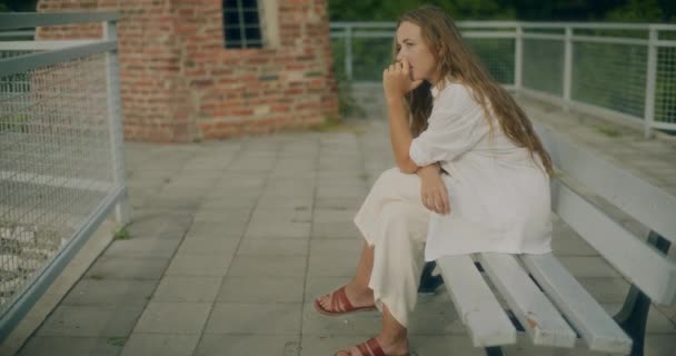 Hidasliikkeinen laukaus masentunut nuori nainen käsi leualla istuu penkillä lähellä kaide - Materiaali, video