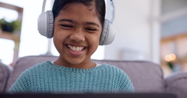 Girl kid, laptop and headphones on sofa, laugh and watch funny video with audio tech in living room. Child, listening and computer with music, streaming subscription or comedy movie in family house. - Footage, Video