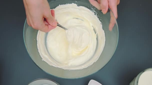 Le mani femminili mescolano con un cucchiaio una massa cremosa tenera e liscia per una torta. Vista dall'alto del tavolo della cucina. Cucinare in cucina - Filmati, video