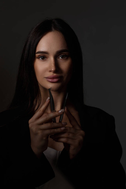 beauty professional woman holding tweezers while posing on black background - Fotografie, Obrázek