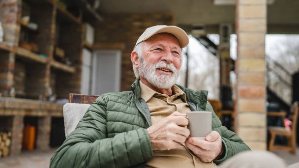 Un hombre mayor se sienta al aire libre en otoño día mantenga taza de café o té - Foto, imagen