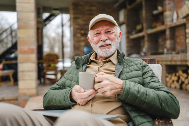 Un homme âgé assis en plein air en automne jour tenir tasse de café ou de thé - Photo, image