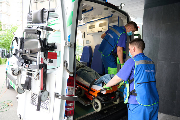 Sanitäter in Schutzmasken entladen den Patienten aus dem Krankenwagen, der Patient wird auf einer speziellen Trage fixiert - Foto, Bild
