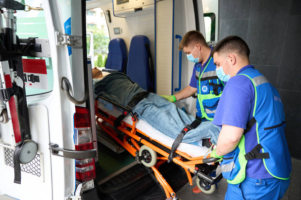 Junge Sanitäter entladen einen Patienten aus einem Krankenwagen, der Patient wird auf einer speziellen Trage fixiert - Foto, Bild