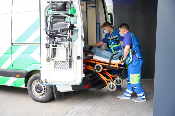 Erkek sağlık görevlileri kazada kurbanı ambulanstan indiriyor, hasta özel bir sedyeye bağlanıyor. - Fotoğraf, Görsel