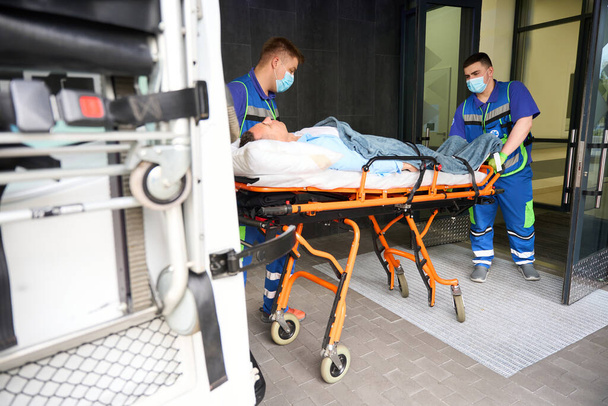 Άνδρες νοσοκόμοι παρέδωσαν το θύμα στα Επείγοντα. Ο ασθενής τοποθετήθηκε σε ειδικό φορείο. - Φωτογραφία, εικόνα
