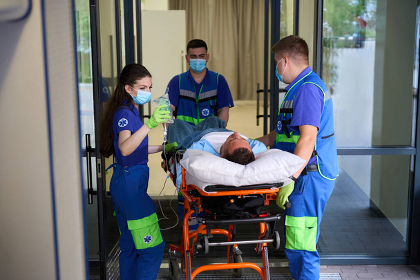 Лікарі швидкої допомоги відвезли чоловіка в лікарню швидкої допомоги, пацієнт отримує крапельку з знеболювальними засобами - Фото, зображення