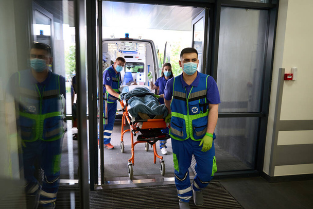 Zespół sanitariuszy dostarczył wózek z pacjentem na pogotowie, personel medyczny pracujący w maskach ochronnych - Zdjęcie, obraz