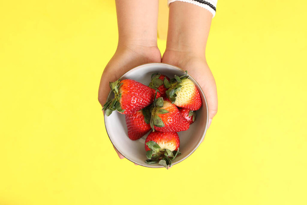 The Asian woman holding strawberry in the hand on the yellow background. - Photo, Image
