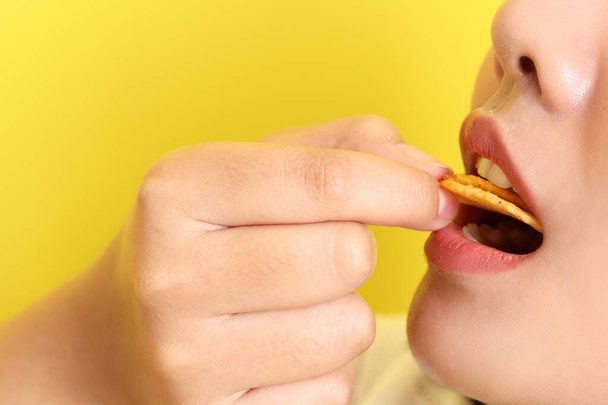 Azjatka jedząca chipsy z ręki na żółtym tle. - Zdjęcie, obraz
