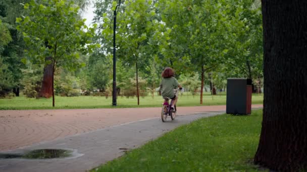 back view madre è felice perché sua figlia è in bicicletta da sola per la prima volta nel concetto di cura del parco infanzia felice - Filmati, video