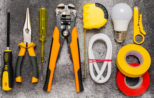 Electrician tools on black marble background.Multimeter,construction tape,electrical tape, screwdrivers,pliers,an automatic insulation stripper, socket and LED lamp.Flatley.electrician concept. - Photo, Image