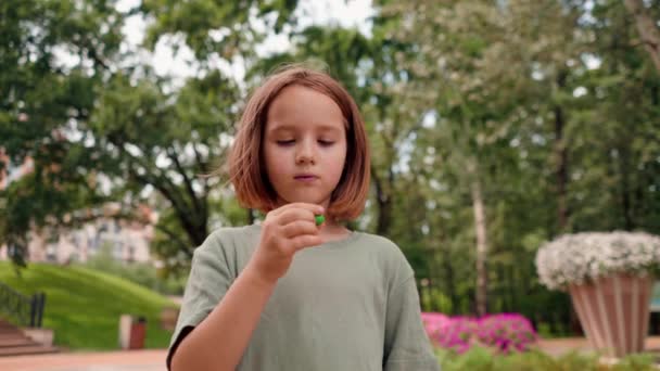 portrét krásná roztomilá dívka jíst malé bonbóny v městském parku šťastný bezstarostné dětství - Záběry, video