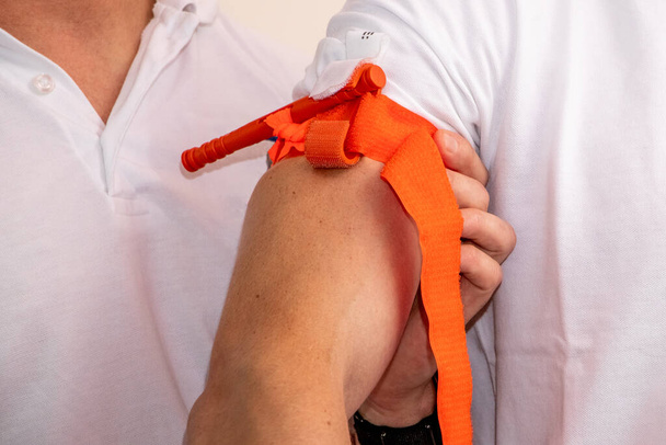 Een gezondheidswerker demonstreert hoe een tourniquet op de arm moet worden aangebracht om te stoppen met bloeden in geval van letsel of ongeval - Foto, afbeelding