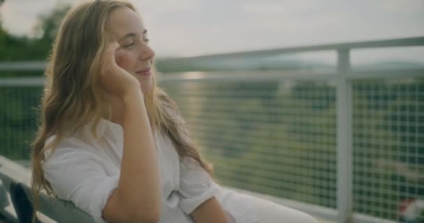 Hidasliikkeinen laukaus hymyilevä vaalea nainen hyväilee hiuksia istuessaan penkillä - Materiaali, video