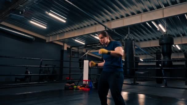 retrato de una boxeadora femenina concentrada en vendajes de boxeo amarillos golpeando a un oponente imaginario en el gimnasio antes de luchar - Imágenes, Vídeo