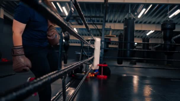 Boxermädchen in Handschuhen klettert an den Seilen in den Boxring in der Turnhalle trainiert vor dem Kampf hart - Filmmaterial, Video