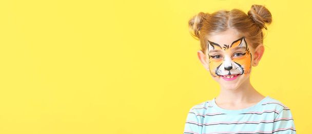 Grappig klein meisje met gezicht schilderen op gele achtergrond met ruimte voor tekst - Foto, afbeelding