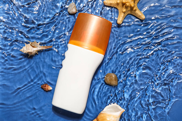 Crema protector solar con estrellas de mar y conchas marinas en agua sobre fondo de color - Foto, imagen