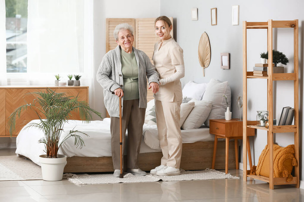 Young caregiver helping senior woman in bedroom - Фото, изображение