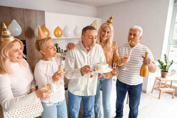 Mature man with his friends making wish at Birthday party in kitchen - Photo, Image