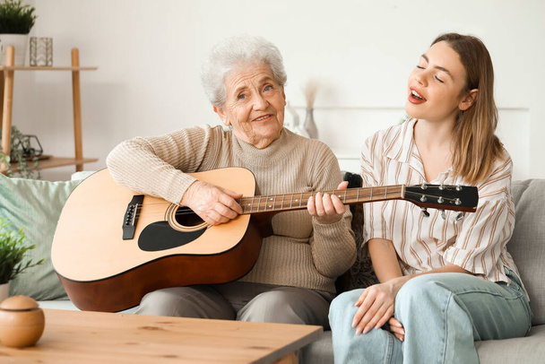 Jeune femme et sa grand-mère jouant de la guitare à la maison - Photo, image