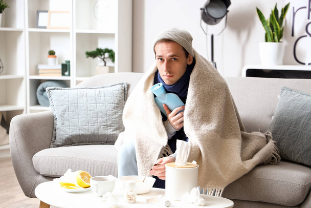 Ill young man with hot water bottle eating soup at home - Photo, Image