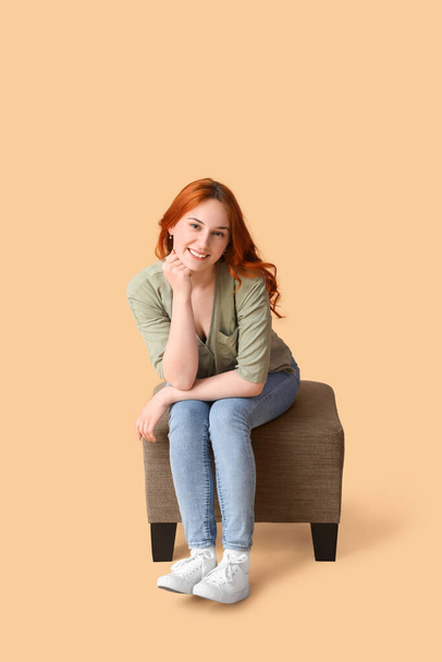 Mujer joven sentada en puf sobre fondo beige - Foto, imagen