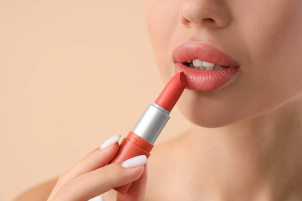 Jeune femme appliquant du rouge à lèvres sur fond clair, gros plan
 - Photo, image