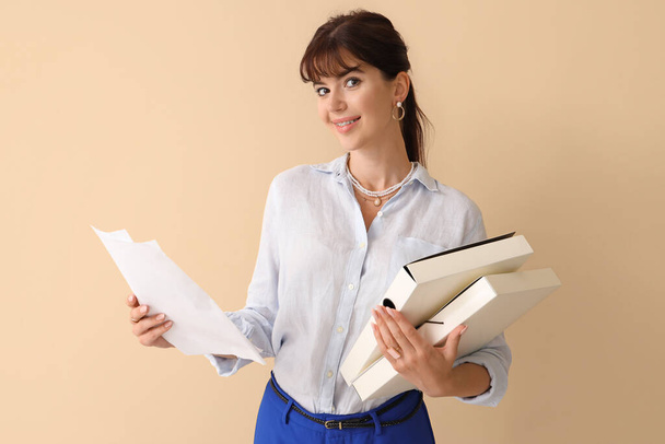 Mooie zakenvrouw met mappen en papieren op beige achtergrond - Foto, afbeelding
