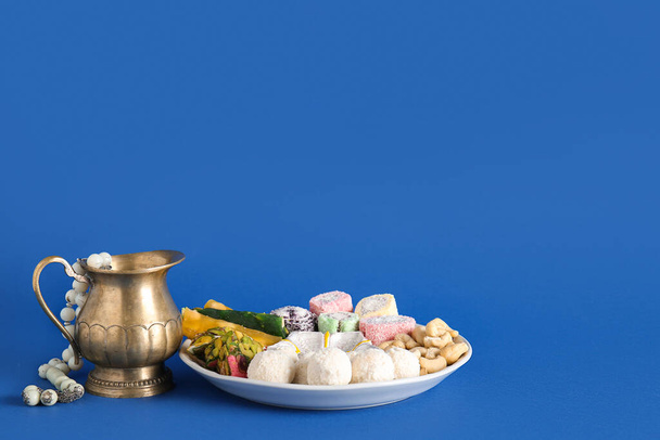 Diya lampa z dzbankiem, koraliki i talerz różnych smakołyków na niebieskim tle. Święto Divaly - Zdjęcie, obraz