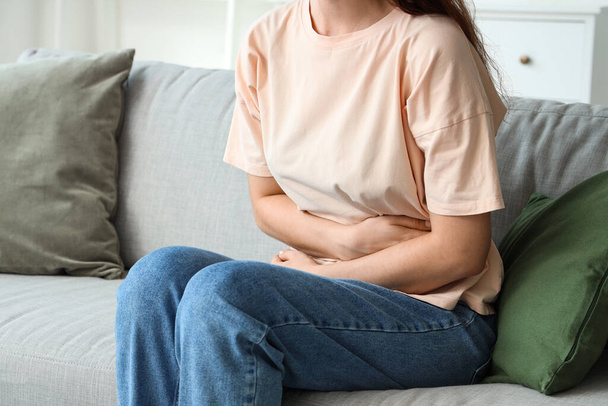 Mladá žena sedí na pohovce a trpí bolestí břicha doma - Fotografie, Obrázek