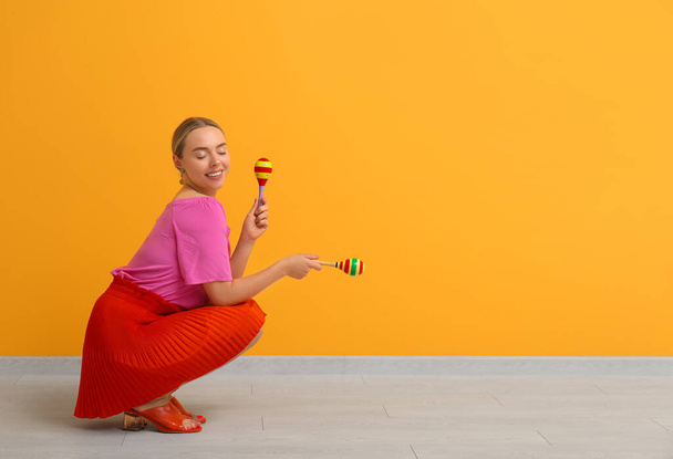 Pretty young woman with maracas on orange background - Фото, изображение
