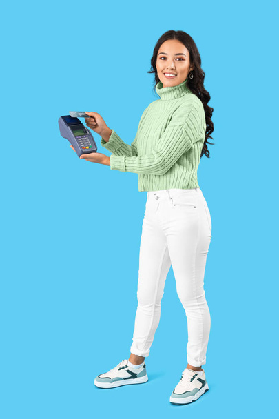Młoda Azjatka z terminalem płatniczym i kartą kredytową na niebieskim tle - Zdjęcie, obraz