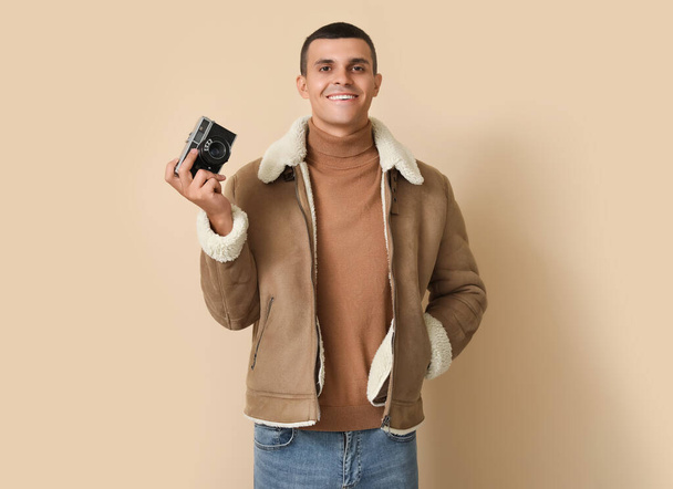Young man in sheepskin jacket with photo camera on beige background - Foto, Bild
